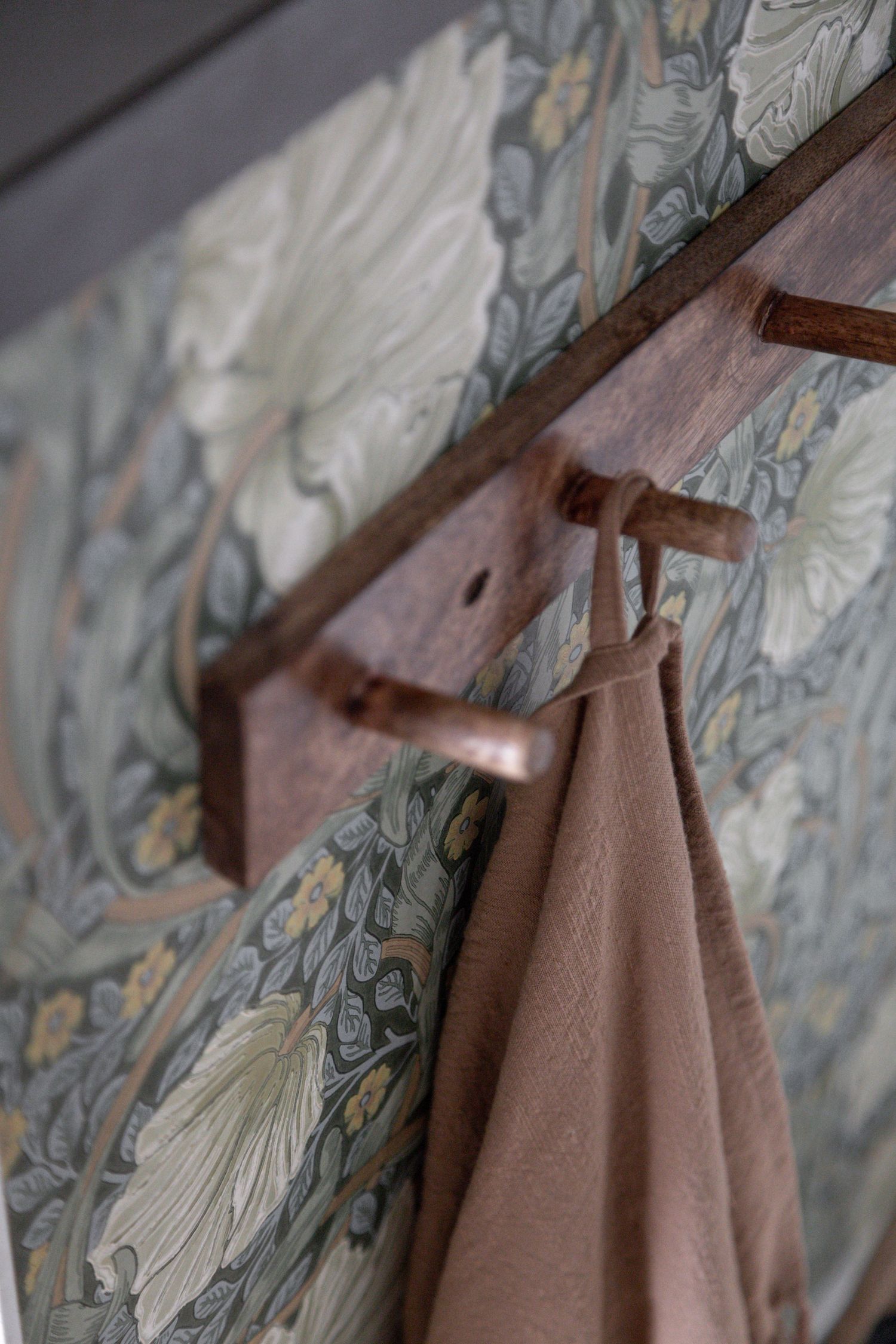 A close-up of a wooden coat hook mounted on floral wallpaper.