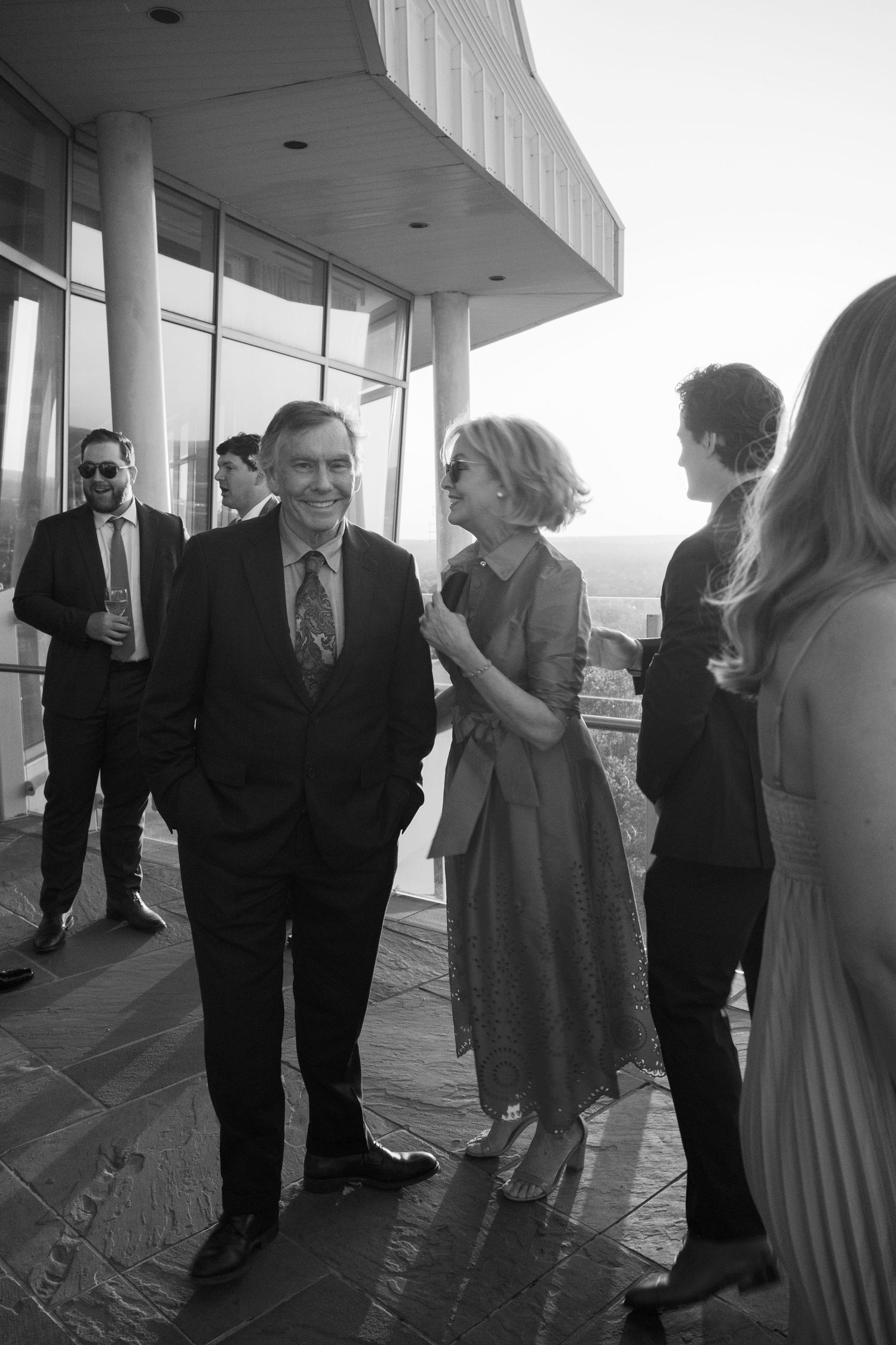 Group of people gathered on a covered outdoor terrace wearing formal attire in black and white at an event.