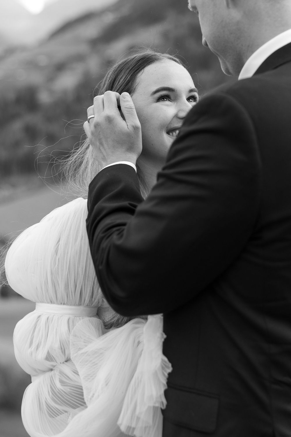 Black and white intimate wedding moment with groom tenderly touching bride's face in formal attire.