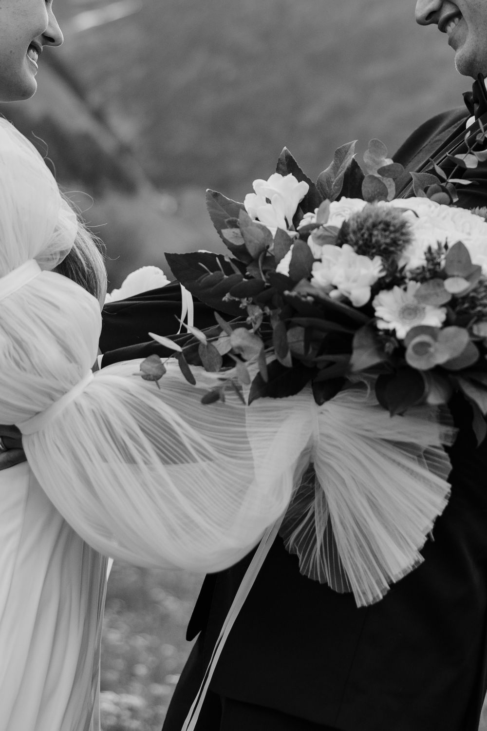 Black and white wedding photo showing the delicate draping of a white bridal gown and bouquet with florals.