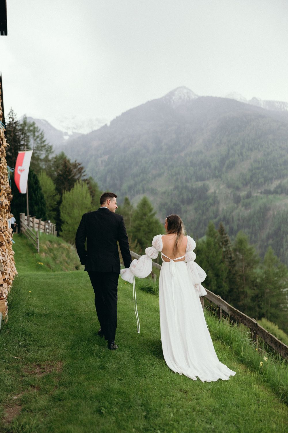 Bride and groom walk hand in hand along a mountain path with scenic alpine views.