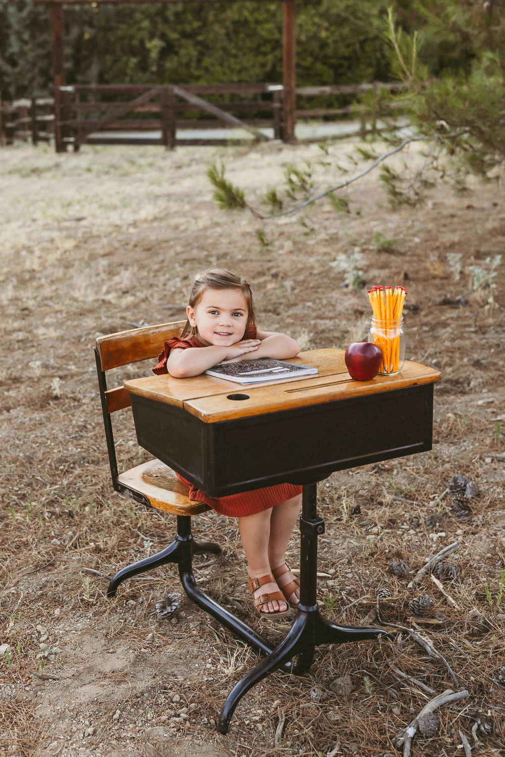 A vintage wooden school desk sits outdoors with supplies and decorative items arranged on its surface.