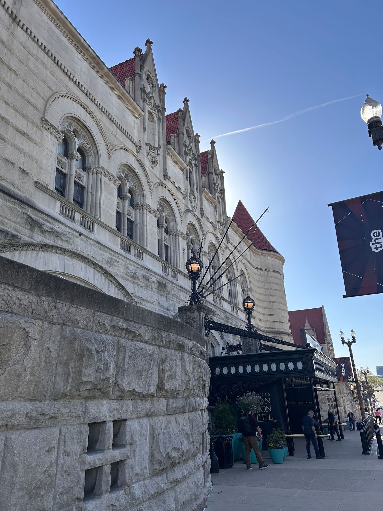 Historic stone building with ornate arched windows and decorative peaks along its facade features vintage lampposts on a city street.
