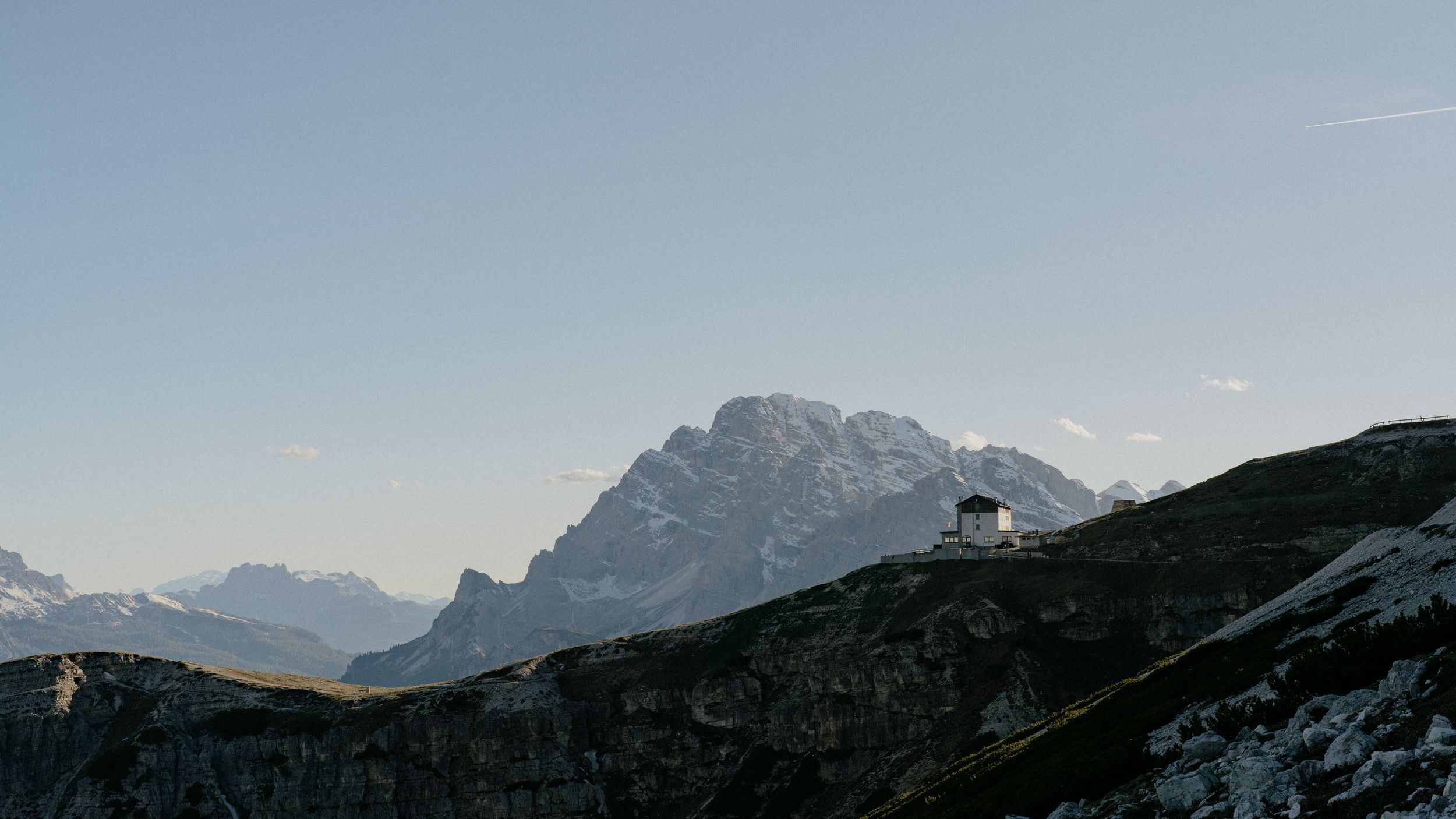Snow-covered ridge beneath towering vertical limestone cliffs in the dramatic mountain landscape of the Dolomites.