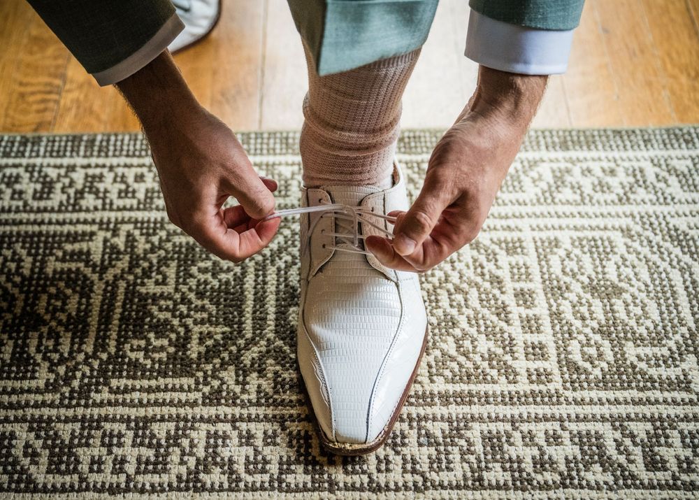 Close-up view of hands tying white dress shoe laces on a patterned area rug.