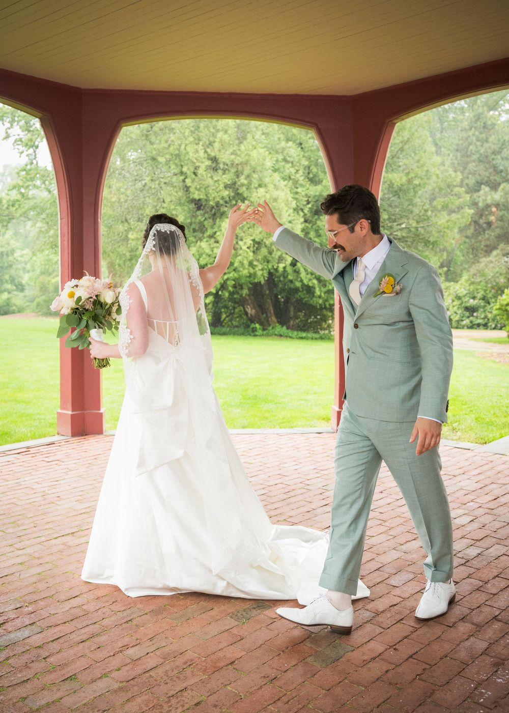 Wedding couple shares a playful dance moment on a brick patio under a covered outdoor space.