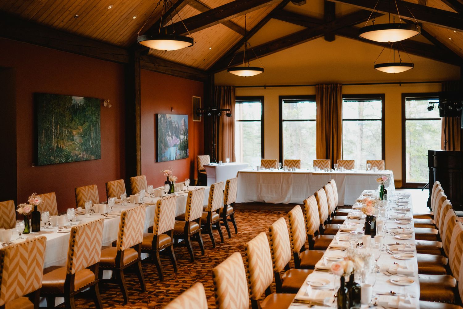 Elegant banquet hall at Stewart Creek Golf Course in Canmore, featuring long tables with floral decorations and scenic artwork on the walls.