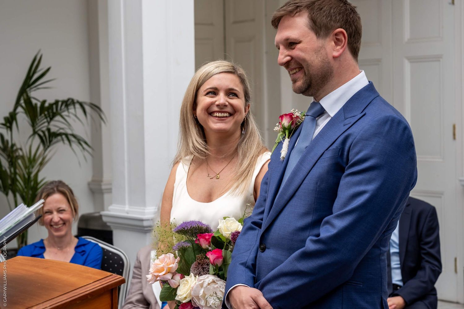 Two people stand together at the front of a venue sharing a joyful moment during a ceremony.