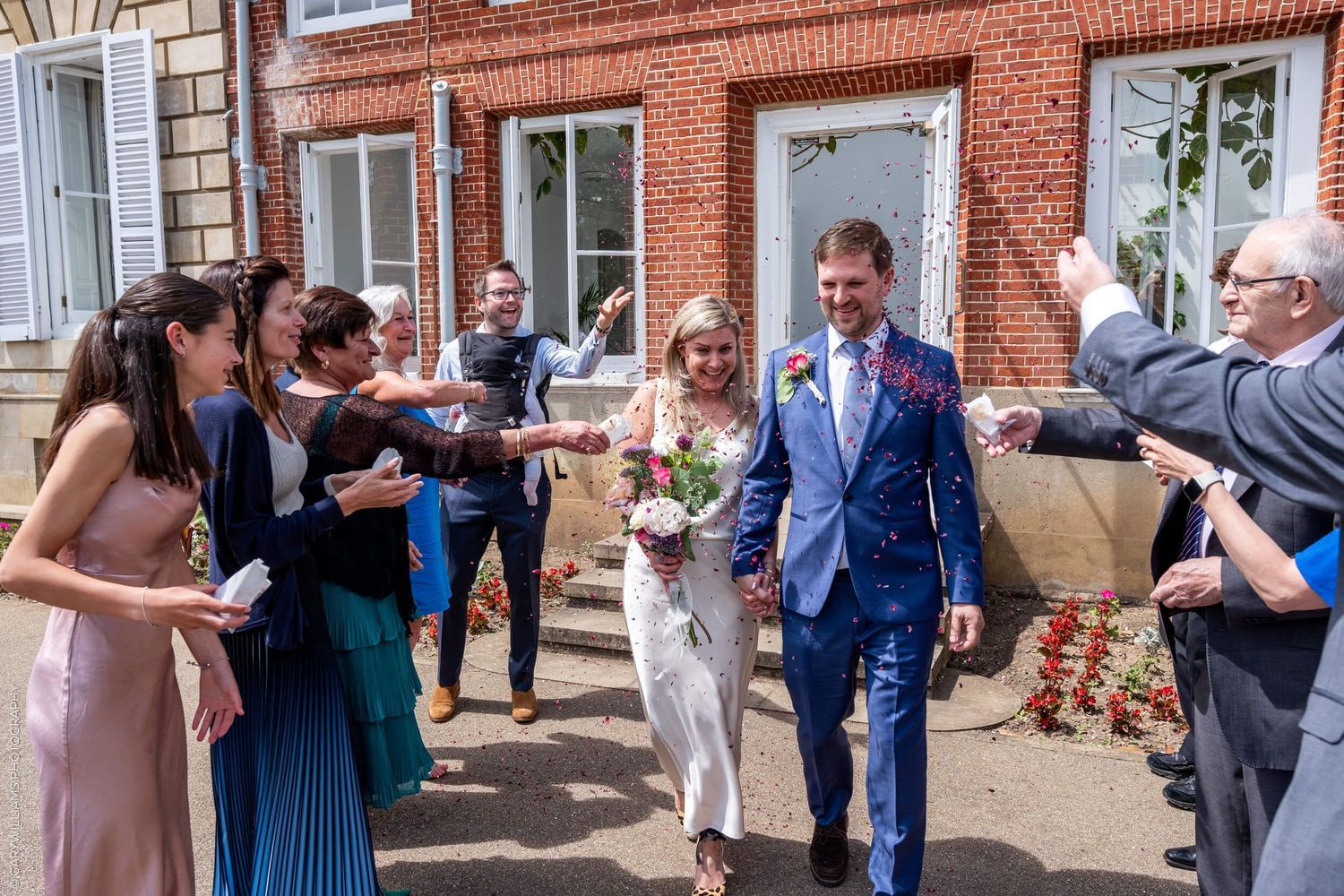 Celebratory group standing outside a brick building toasting and spraying champagne during a festive gathering.