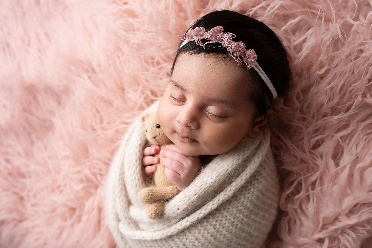 Newborn photography session with pastel pink fluffy backdrop captures peaceful sleeping moments.