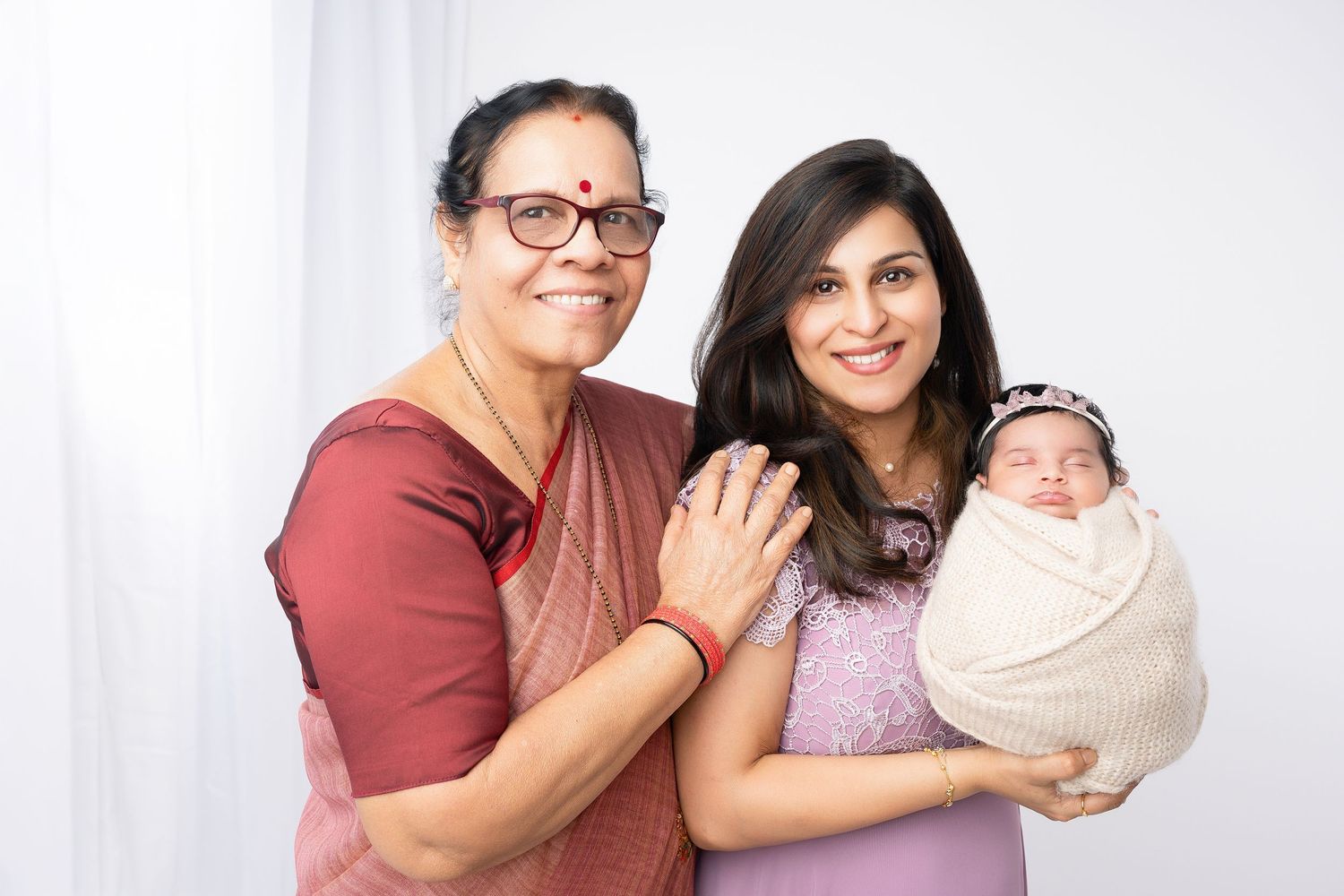 Three generations pose together with newborn baby in studio setting.