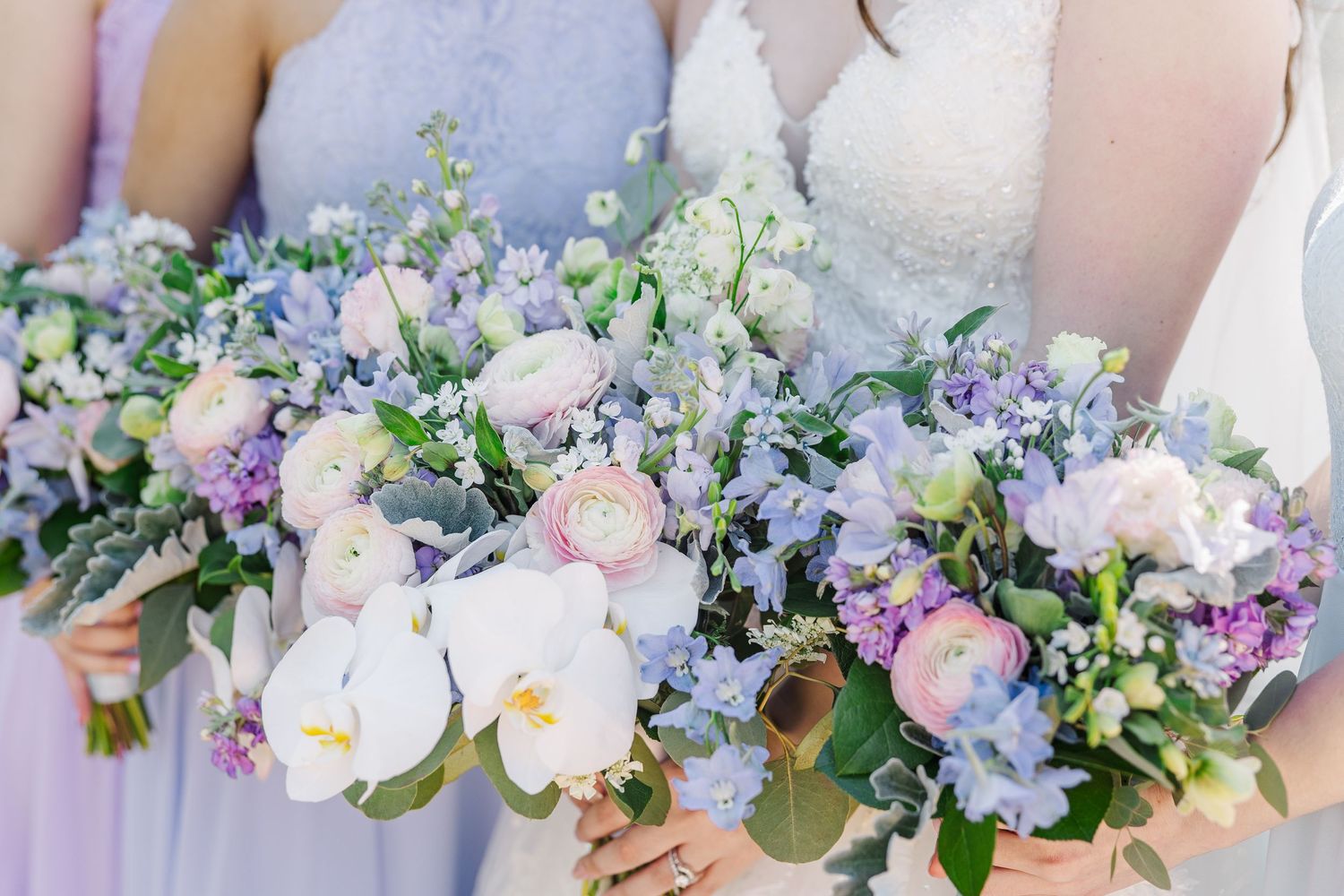 Beautiful wedding bouquets featuring pink peonies, white orchids, purple hydrangeas and delicate greenery held in soft natural light.