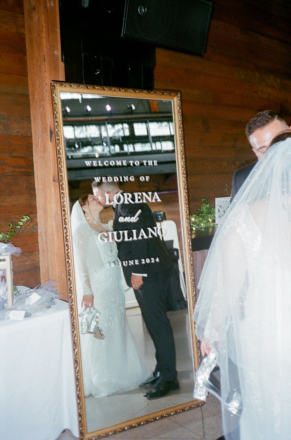 Wedding welcome sign reflection in a mirror showing the couple's names and date.