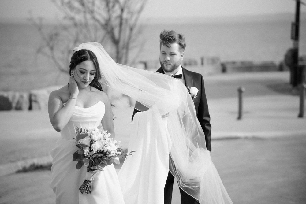 Black and white photo of a bride's veil flowing in the wind during outdoor wedding portraits.