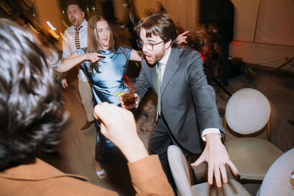 Wedding guests dance enthusiastically at a reception with balloons and party lights.