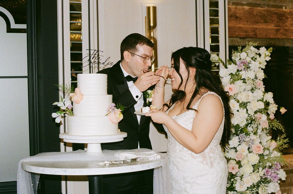 Newlyweds sharing cake during traditional wedding cake cutting ceremony surrounded by floral decor.