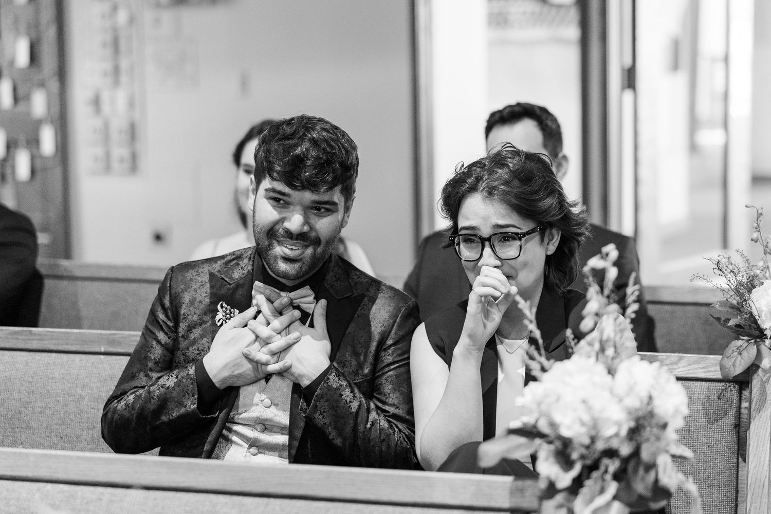 A joyful couple shares a candid laugh together while sitting on a wooden bench, captured in black and white.