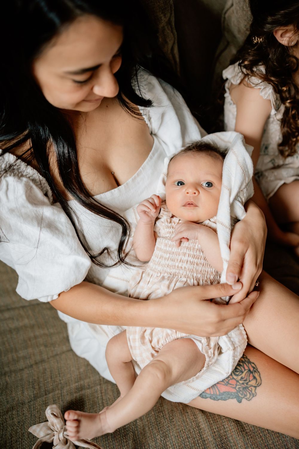 A tender moment between parent and baby in white outfits resting together on a couch.
