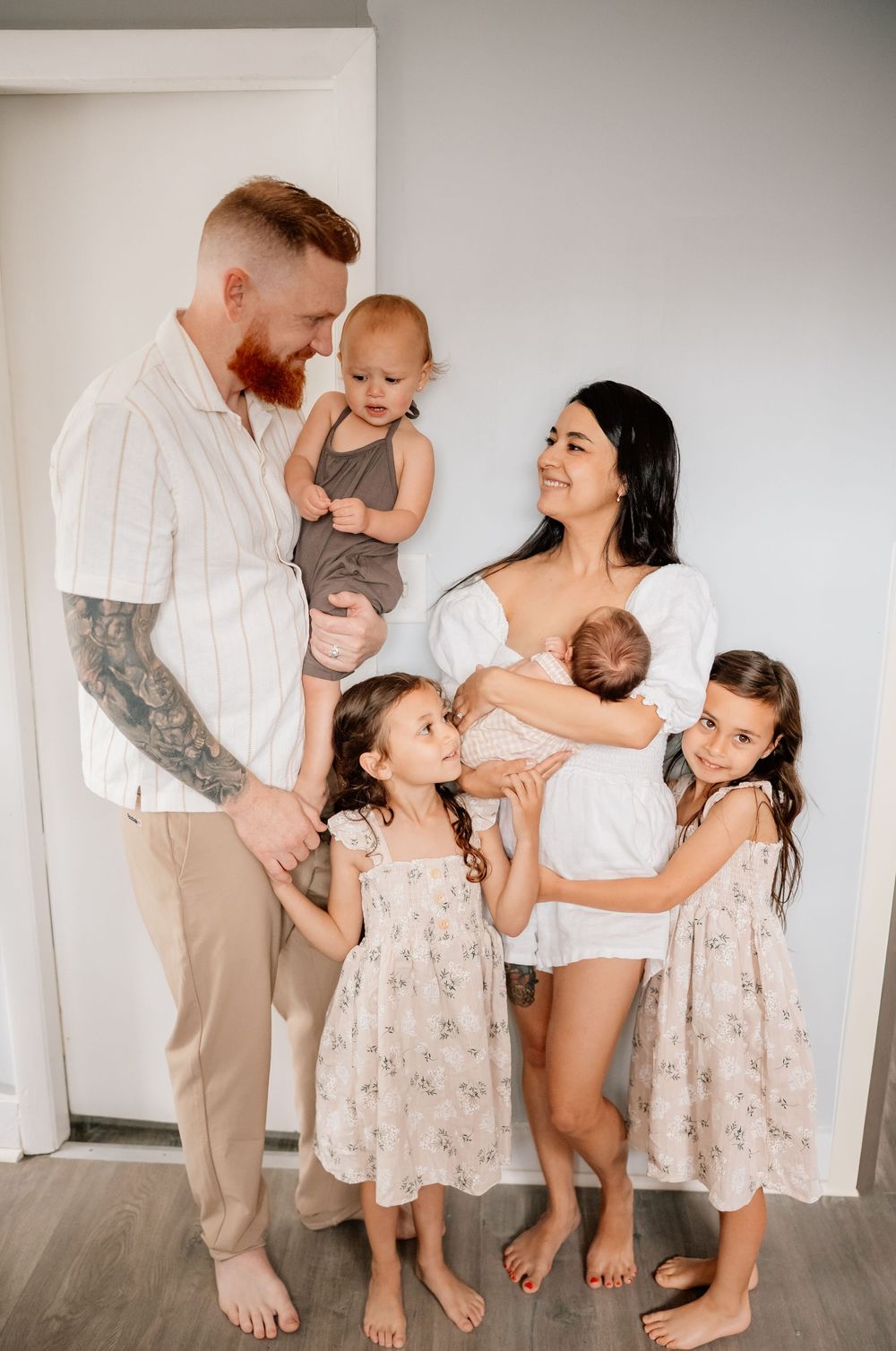 Family of six poses together in a light and airy interior, wearing coordinated white and neutral outfits.