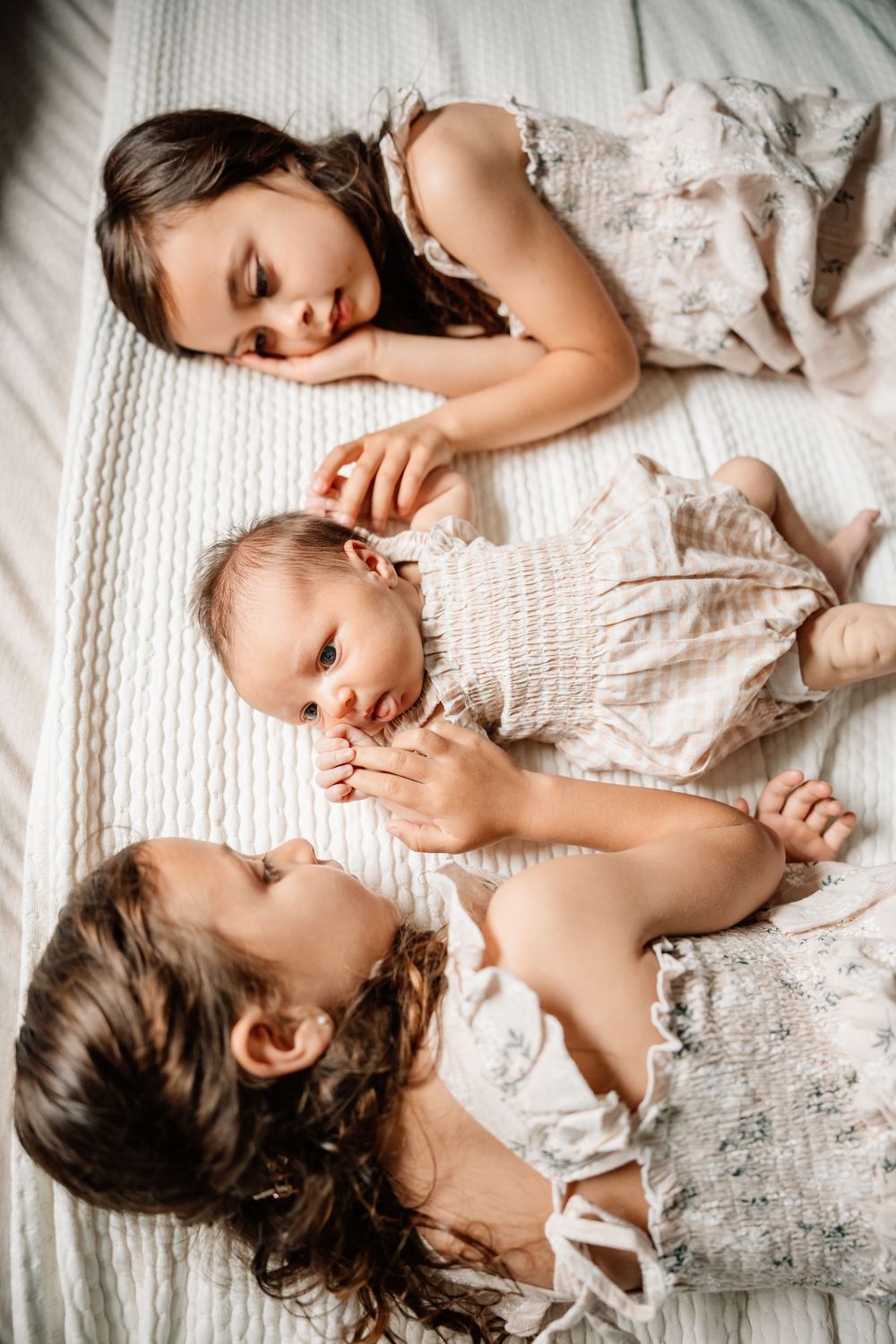 Three people in white outfits lying together on a bed, creating an intimate and peaceful family moment.