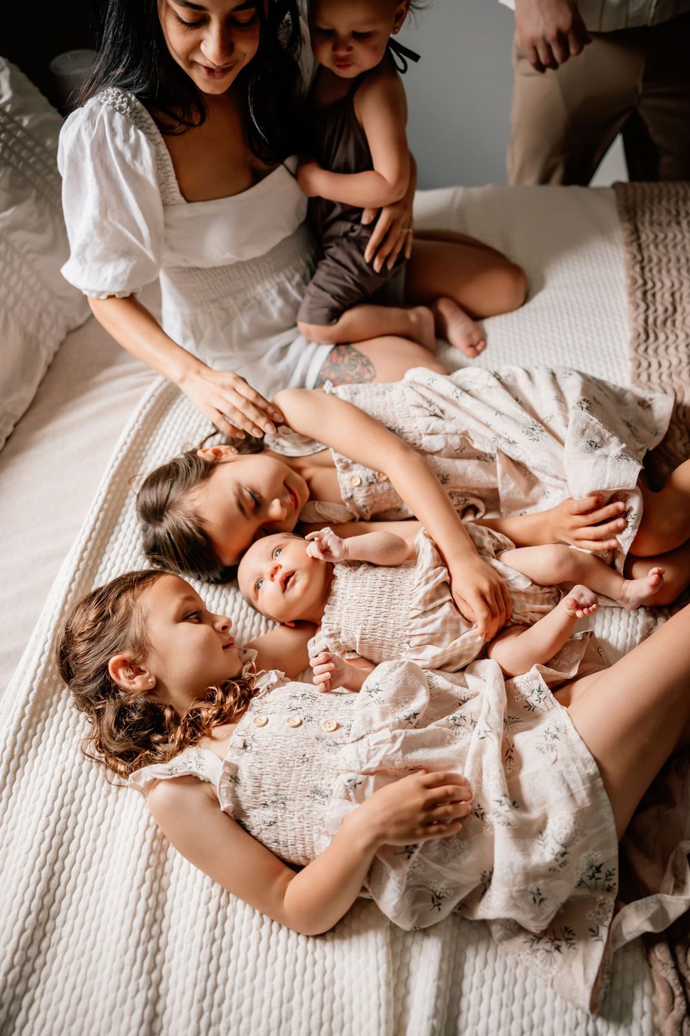 A loving family moment captured on a white bed as everyone cuddles together in soft white dresses.