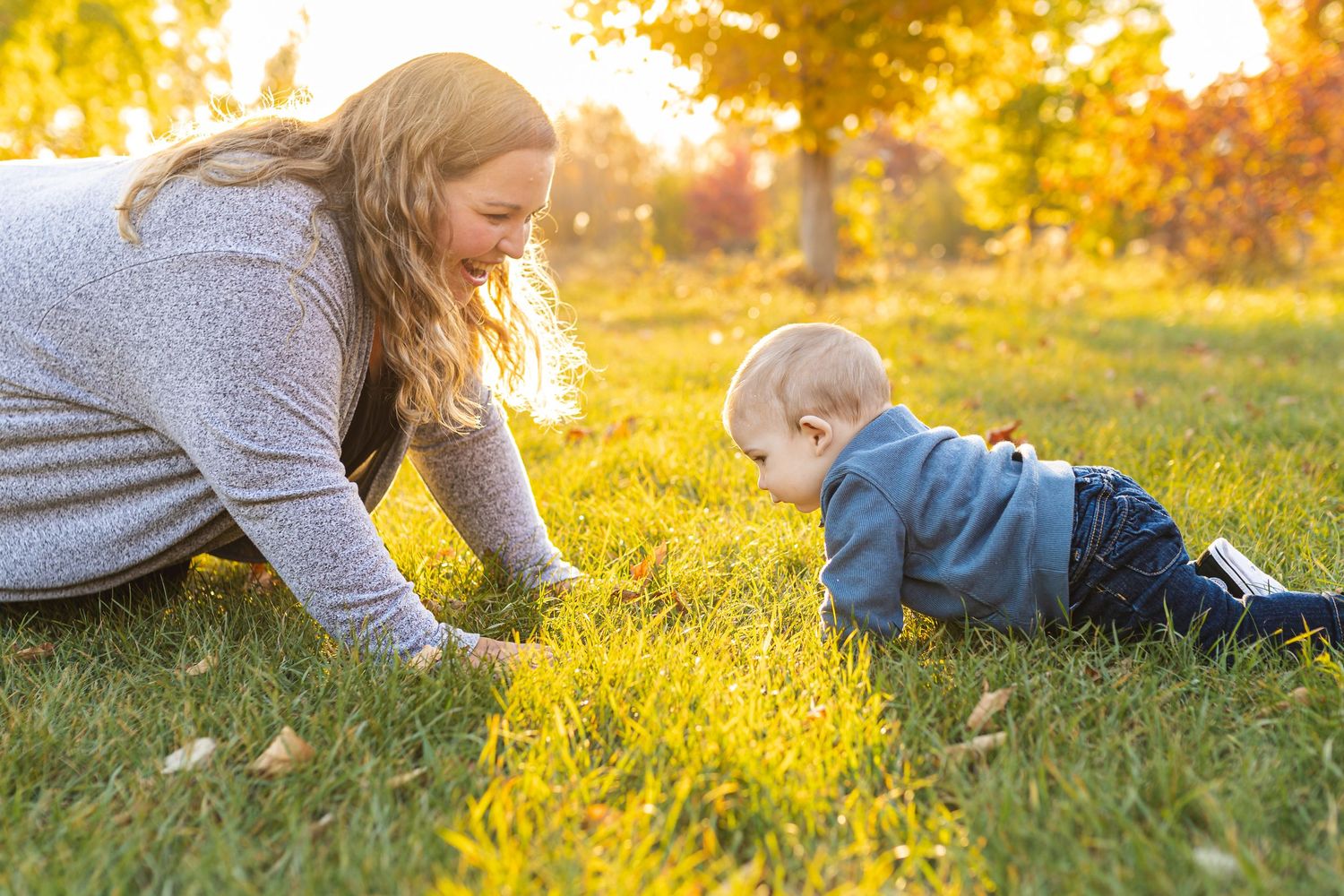 A mom and baby on their hands and knees playing together on green grass during golden sunset hour at Pittock Conservation Area.