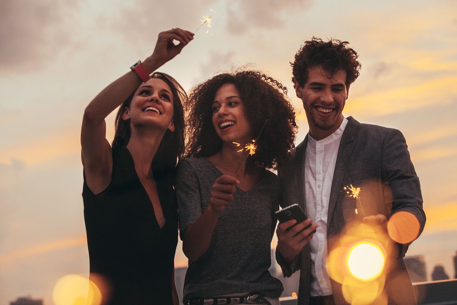 Friends enjoying a rooftop party during sunset with bokeh lights in the background.