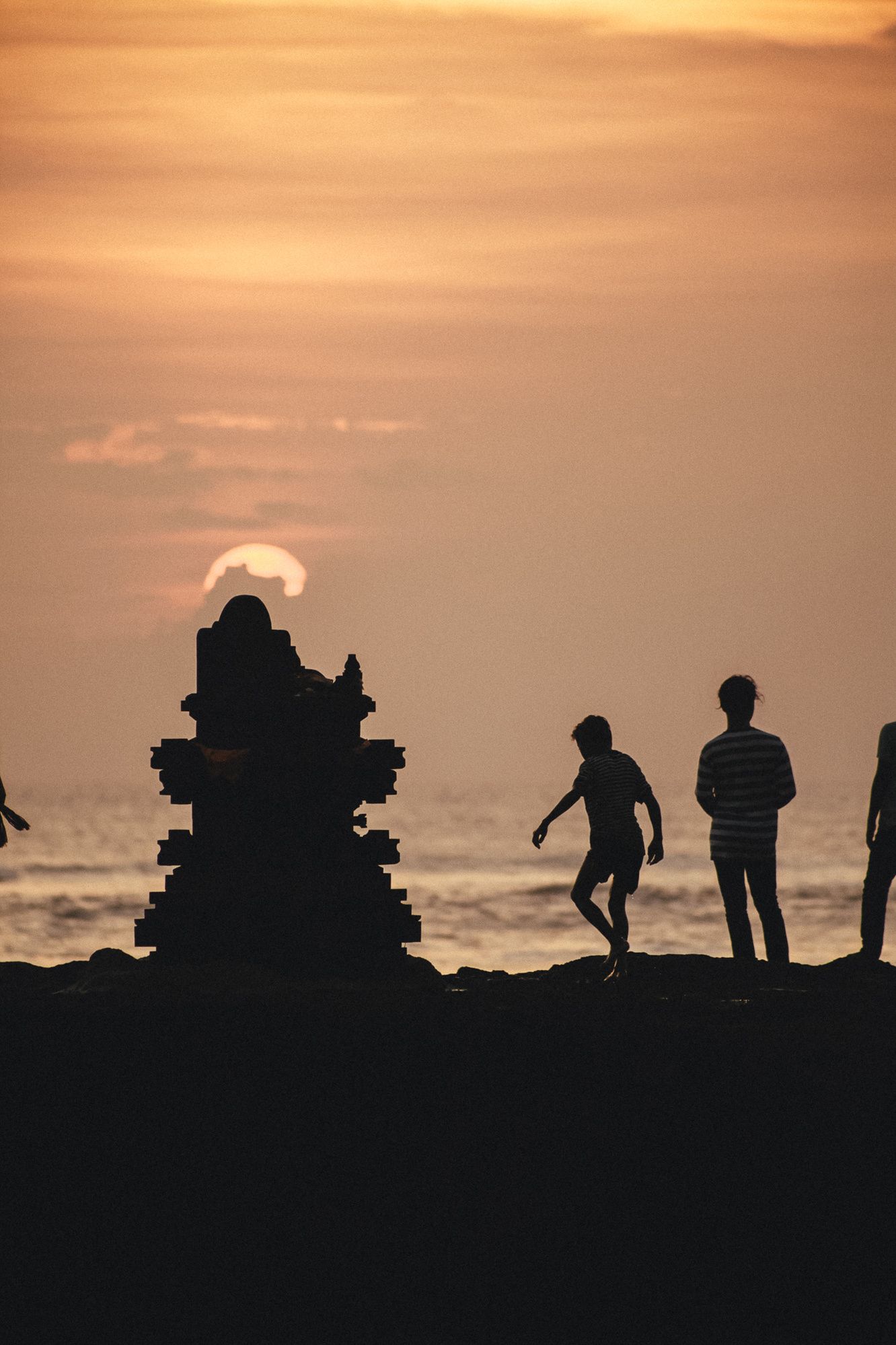 Silhouettes of people standing by ancient ruins against a dramatic sunset over the ocean.