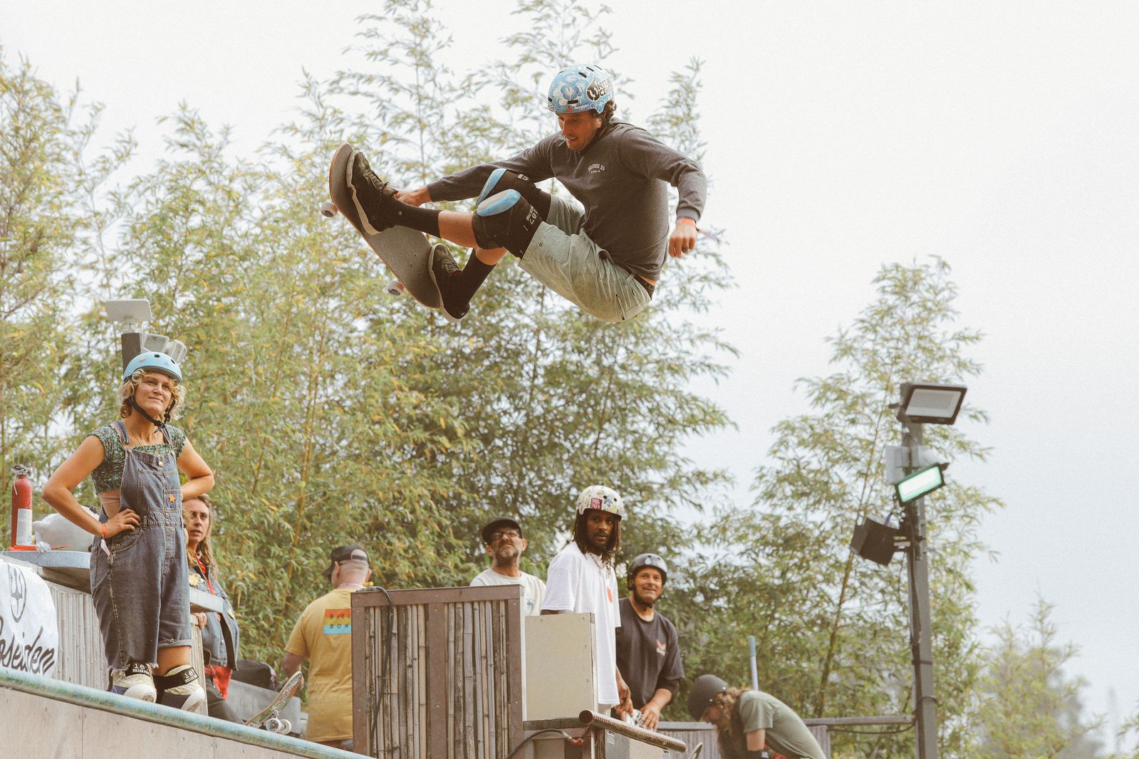 A skateboarder performs a dramatic mid-air trick on a ramp while others watch from below.