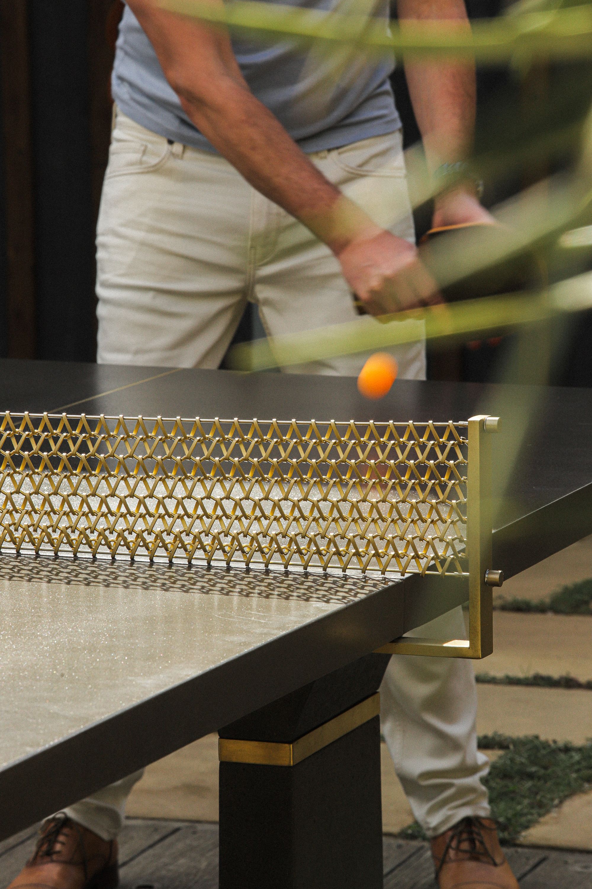 Close-up of ping pong table with gold decorative net and person playing.