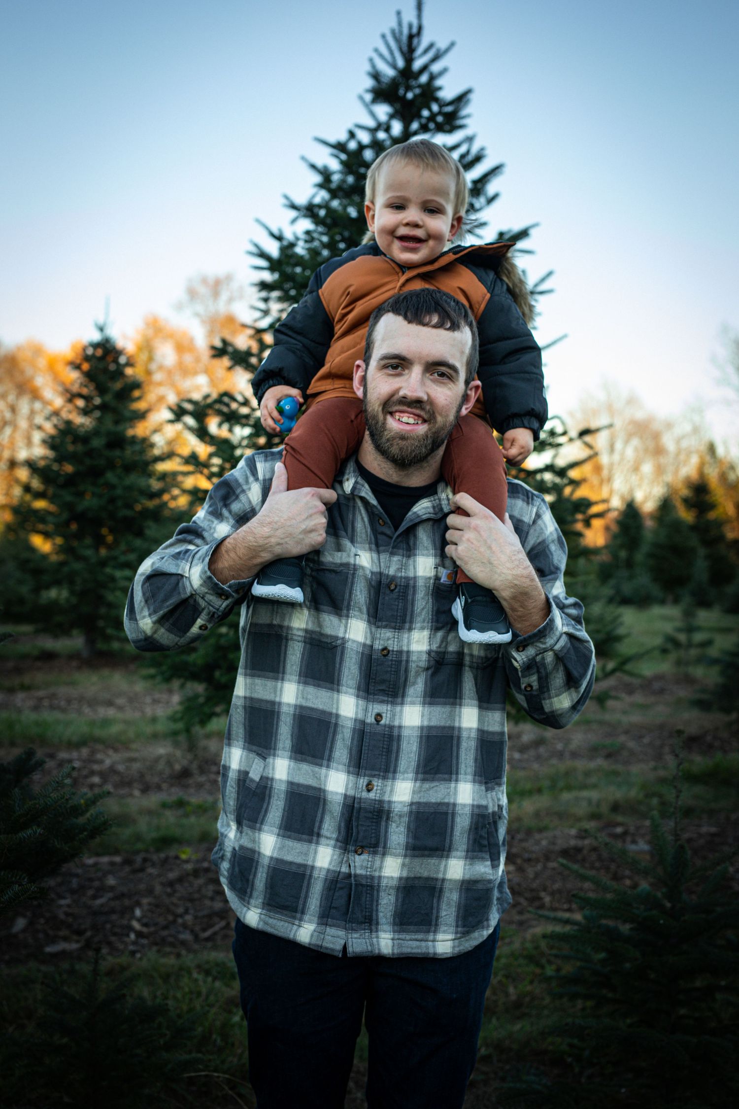 Couple sitting on plaid blanket having romantic moment at Christmas tree farm during sunset.