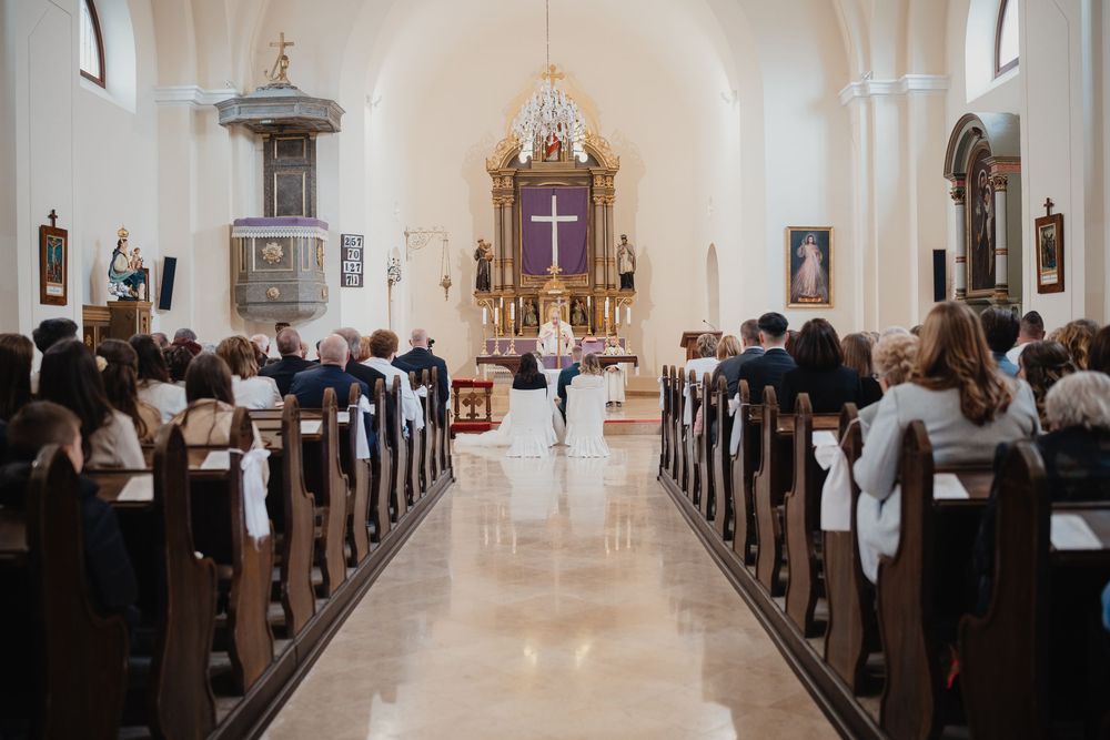 Interior view of a traditional church during a ceremony with congregation seated in wooden pews facing ornate altar.