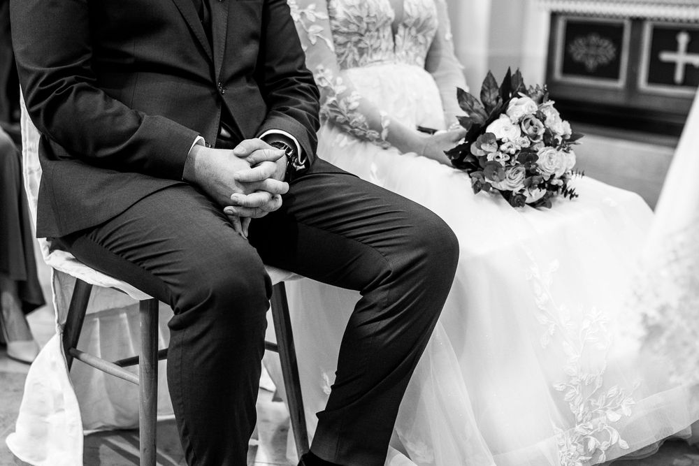 Black and white wedding photo showing couple sitting together with bridal bouquet resting nearby.