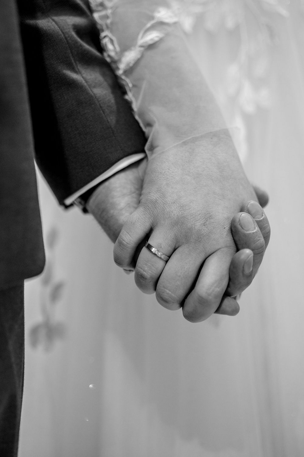 Black and white photograph of a couple holding hands showing their wedding rings against a soft blurred background.