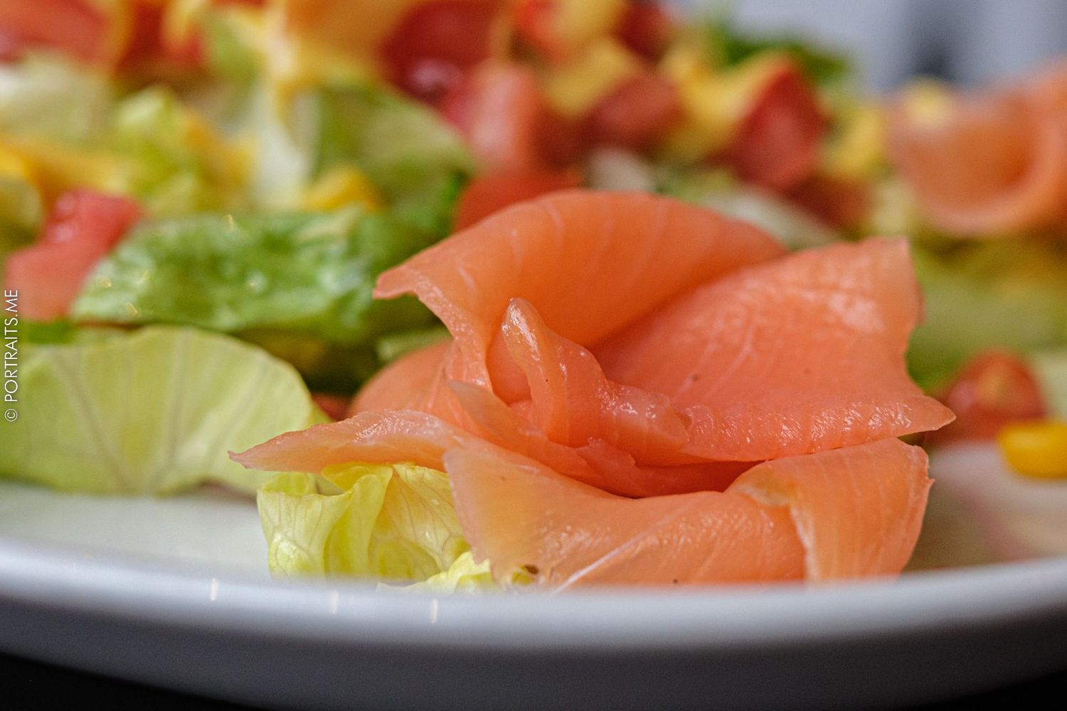 Fresh salmon sashimi served with lettuce on white plate in close-up shot.