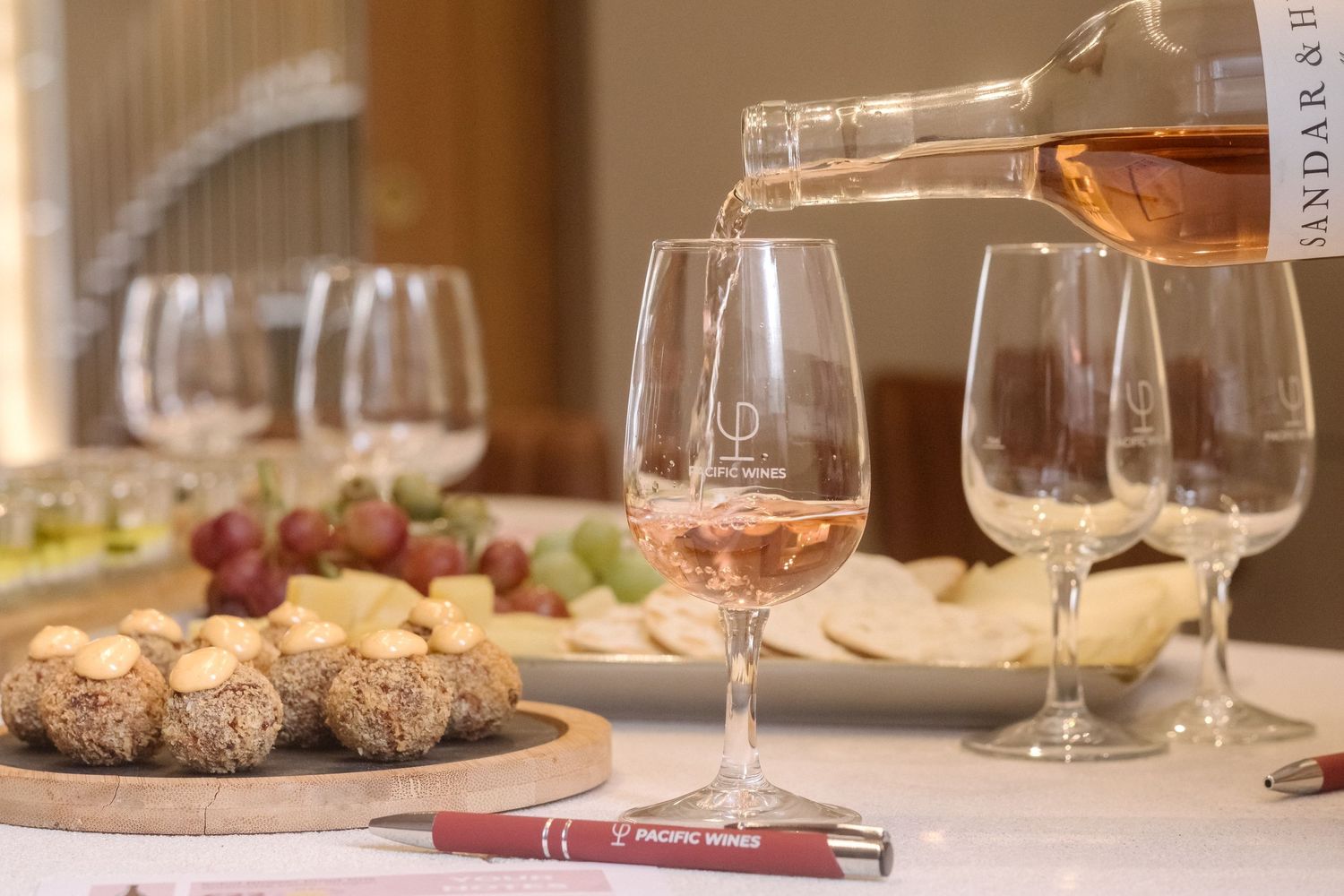 Rose wine being poured into glasses with appetizers and grapes on elegant table setting.