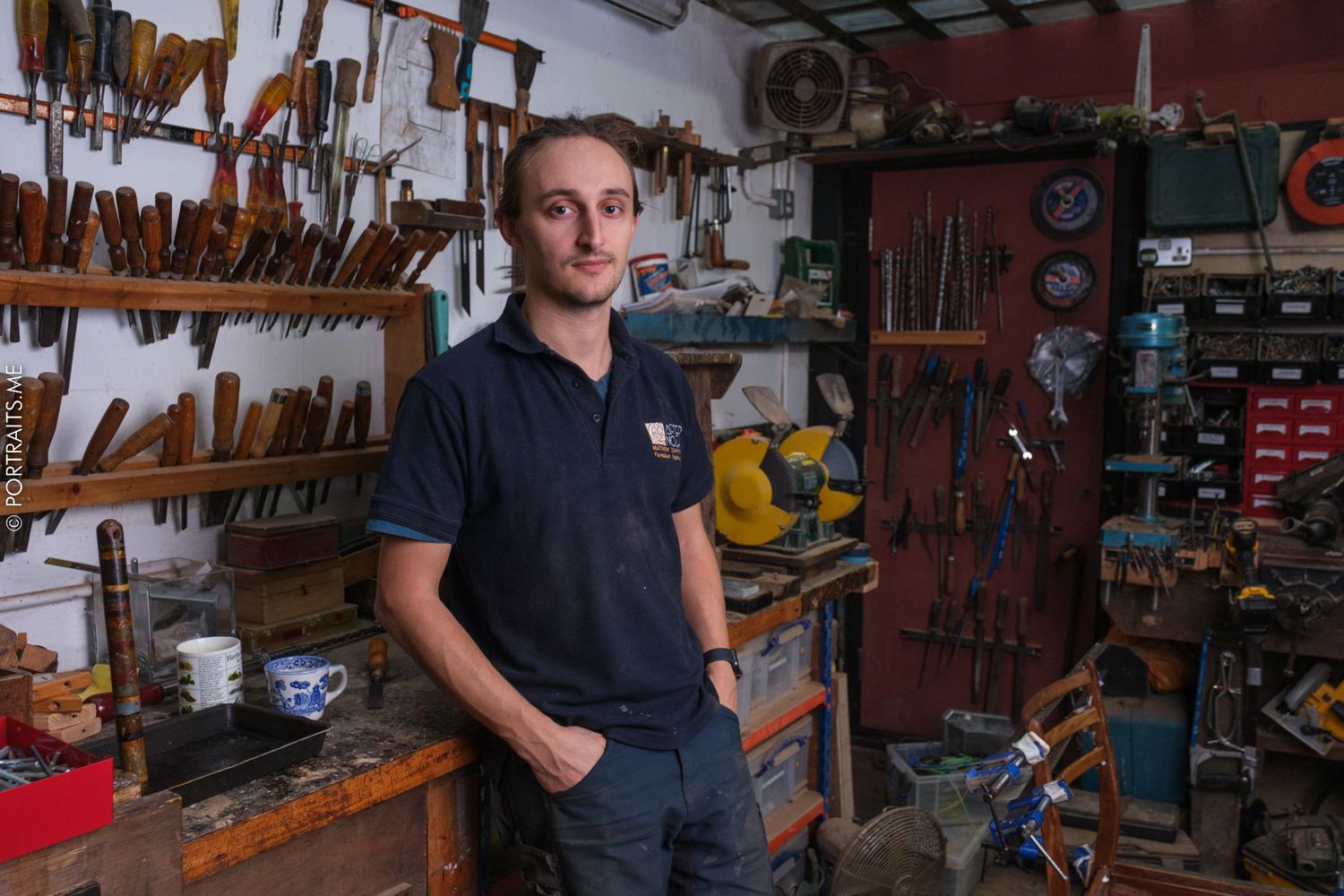 A craftsman stands in a workshop filled with woodworking tools and equipment on display.