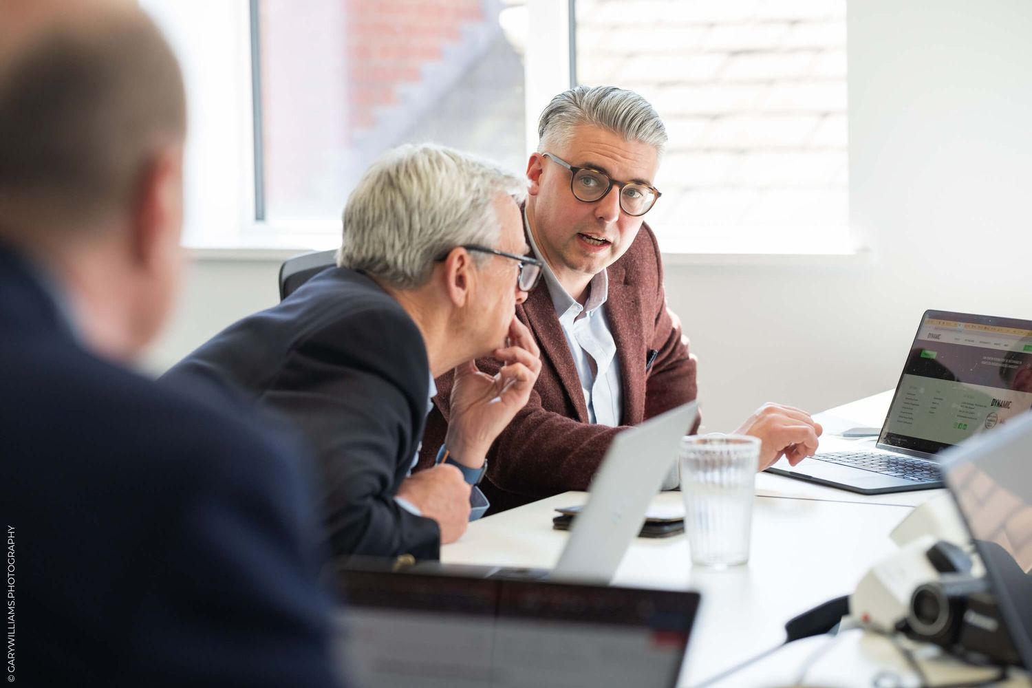 Business colleagues collaborating at a modern office meeting table with laptops and documents.