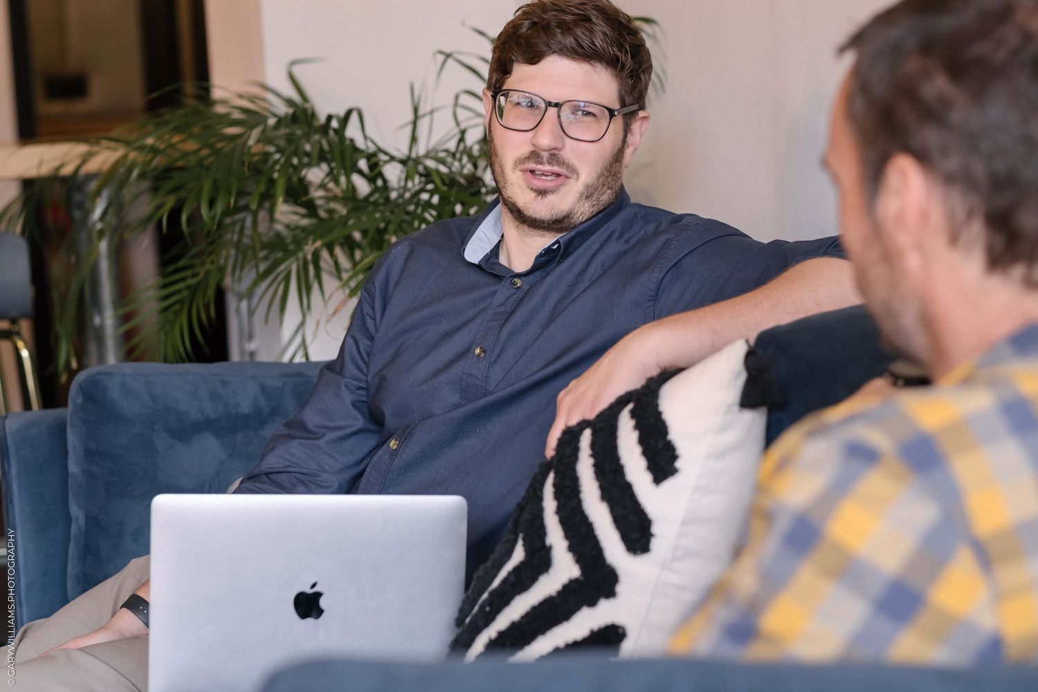 Person in casual attire sitting on couch with laptop during informal meeting.