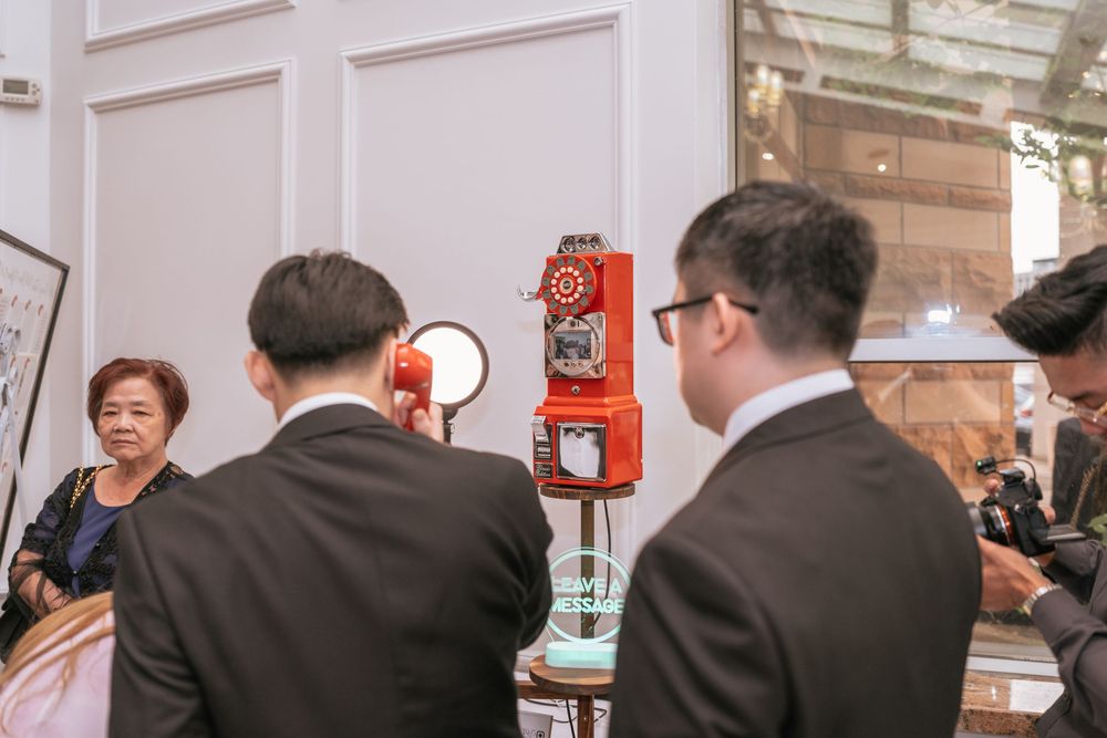 People in dark suits gather around a bright venue space with red emergency equipment mounted on the wall.