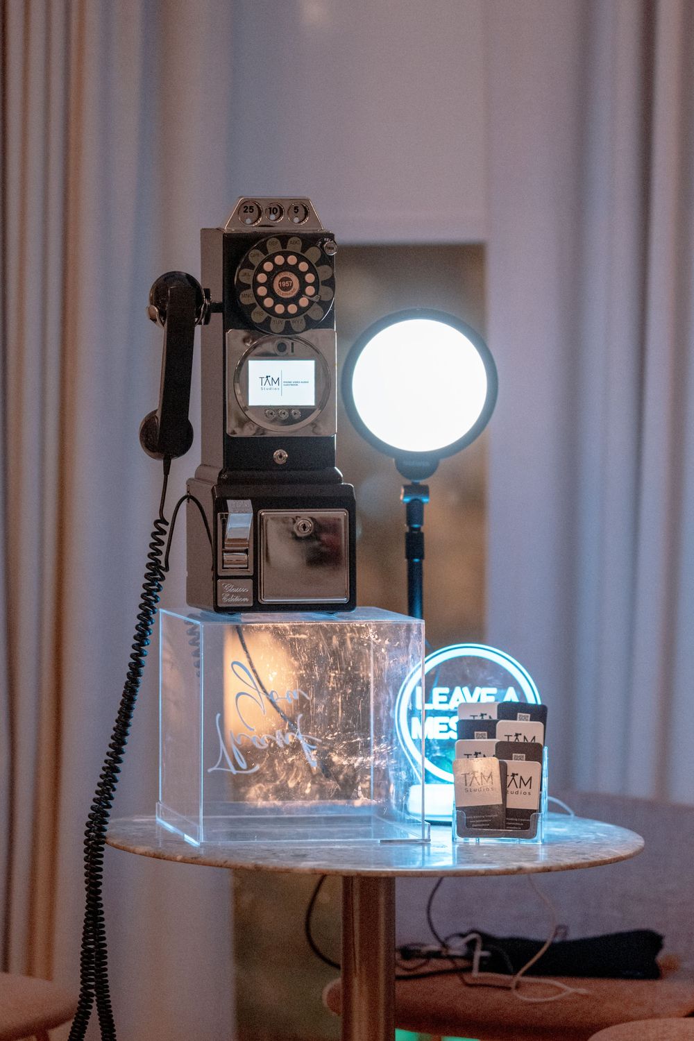 Vintage black rotary payphone on marble table with illuminated neon sign and decorative lighting.