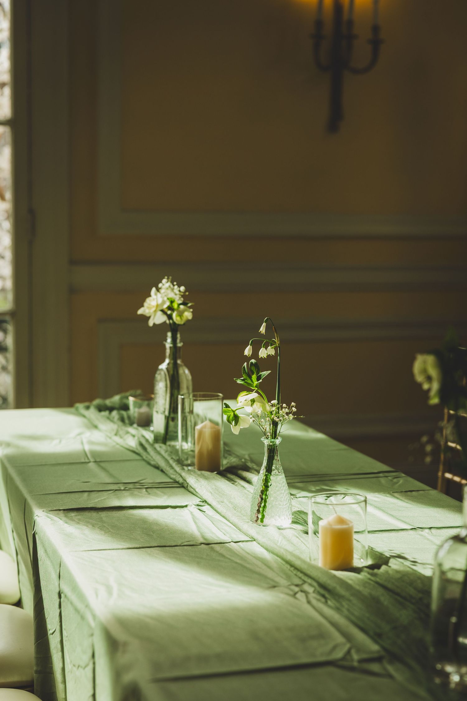 Four elegant place settings on a white tablecloth with natural light and simple floral centerpieces in glass vases.