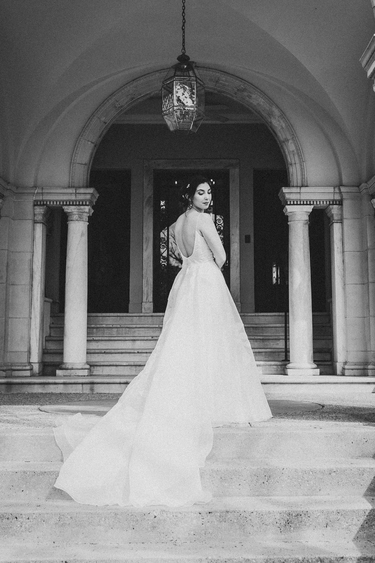 Black and white photo of a bride in a flowing cathedral veil posing under elegant stone arches at the Josephine Butler Parks Center