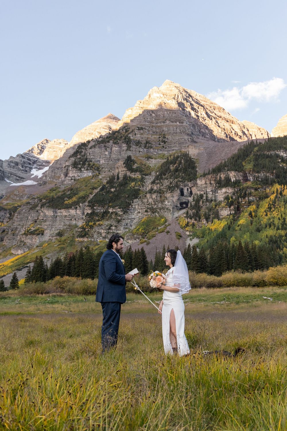 Intimate mountain elopement ceremony set against stunning rocky peaks and autumn foliage in a scenic meadow.