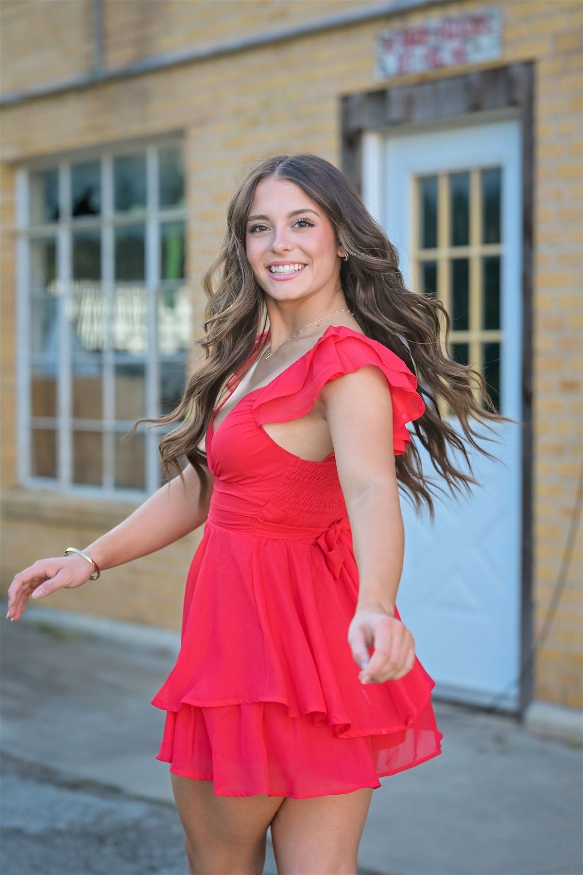 A bright red ruffle dress with cap sleeves photographed in front of a brick building with a blue door.