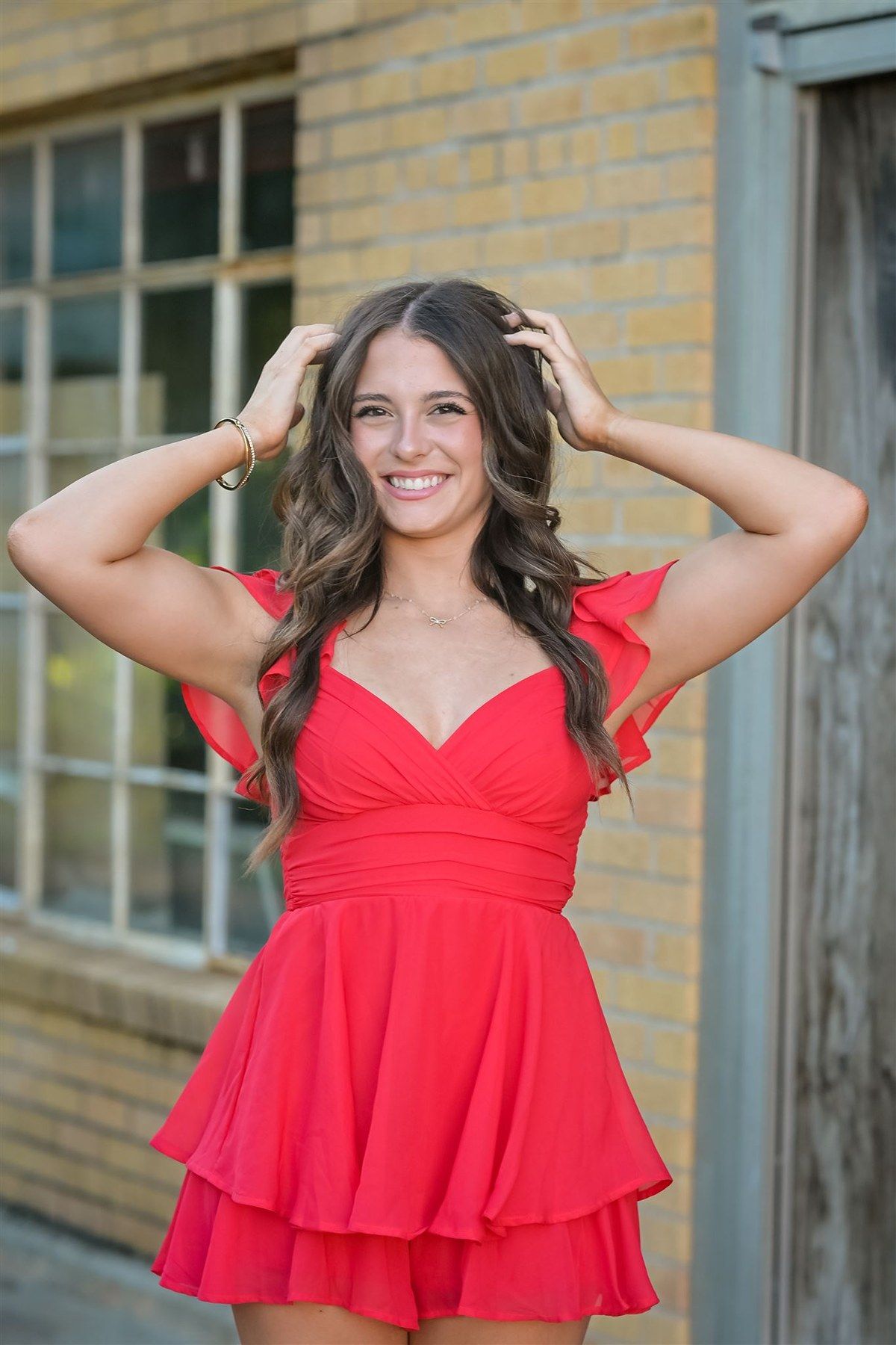 Someone posing outside against a brick wall wearing a bright red ruffled dress with a sweetheart neckline.
