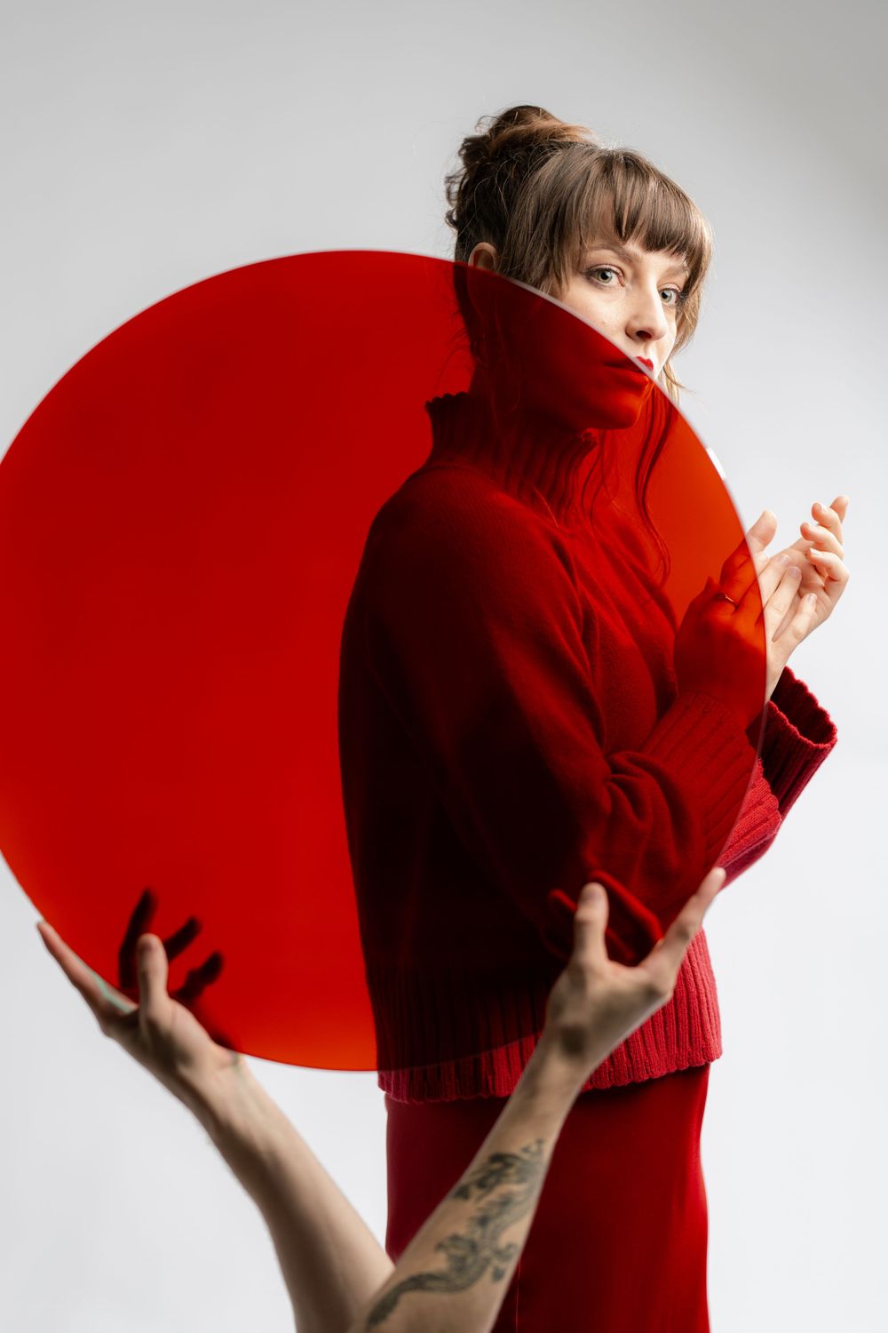 Fashion portrait featuring a red turtleneck sweater against a white backdrop with a large red circular element.