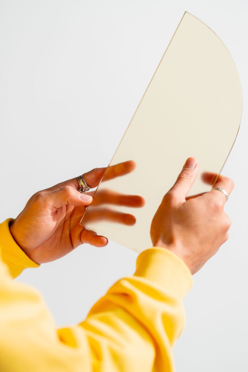 Hands in yellow sleeves holding a blank cream-colored paper or document against a white background.
