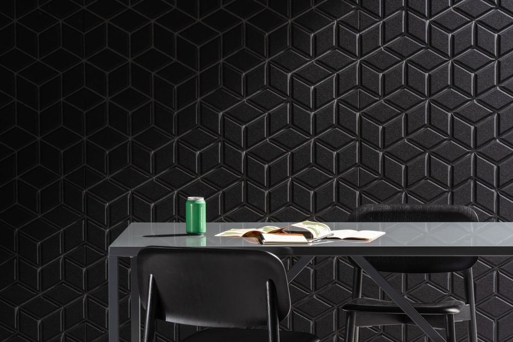 Open book and green drink can on gray desk against modern black geometric wall with hexagonal pattern tiles.