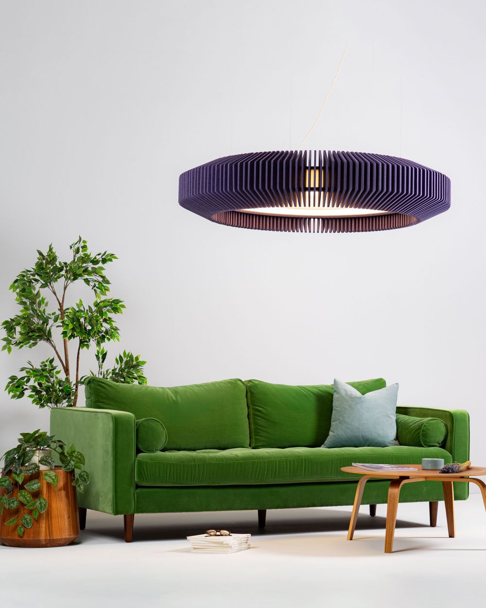 Modern living room with emerald green velvet sofa, wooden coffee table, indoor plant and large purple circular pendant light.
